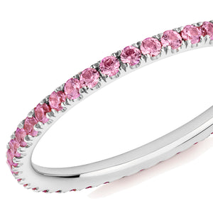 Closeup of a pink sapphire eternity ring in platinum on a white background.