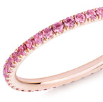 Closeup of a pink sapphire eternity ring in 18ct rose gold on a white background.