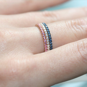 Pink sapphire eternity ring in 18ct rose gold on a hand next to other eternity rings