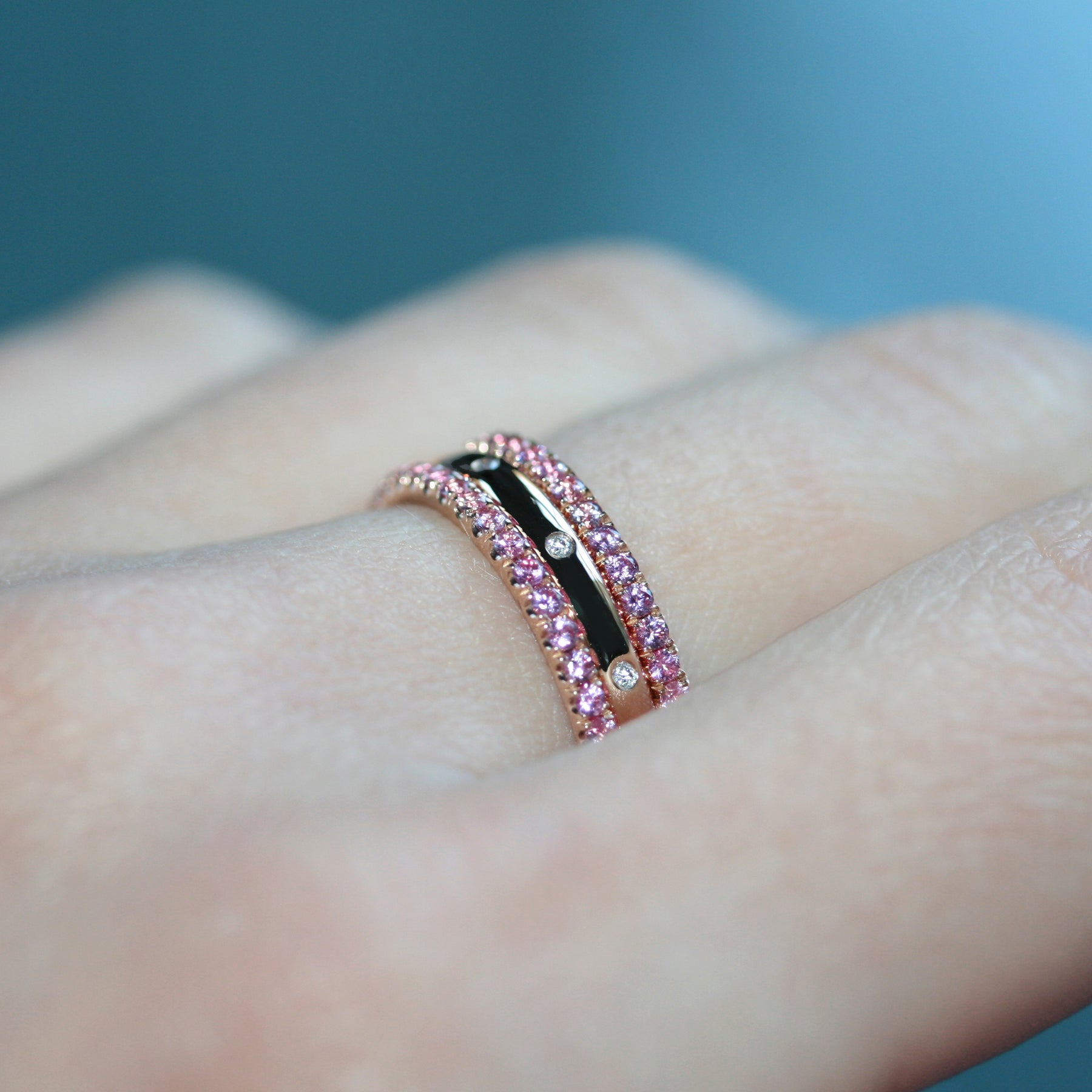 Pink sapphire eternity ring in 18ct rose gold on a hand next to other eternity rings