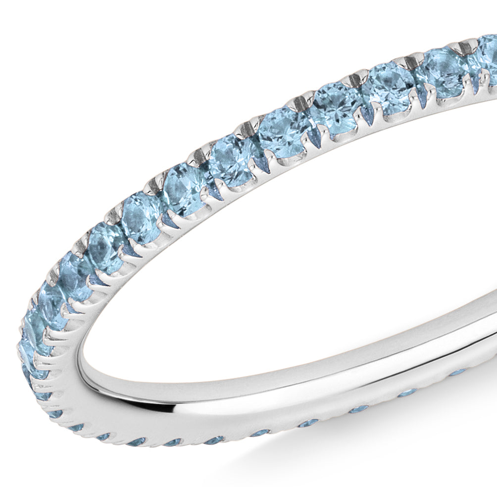 Closeup of a blue Topaz eternity ring in platinum on a white background.