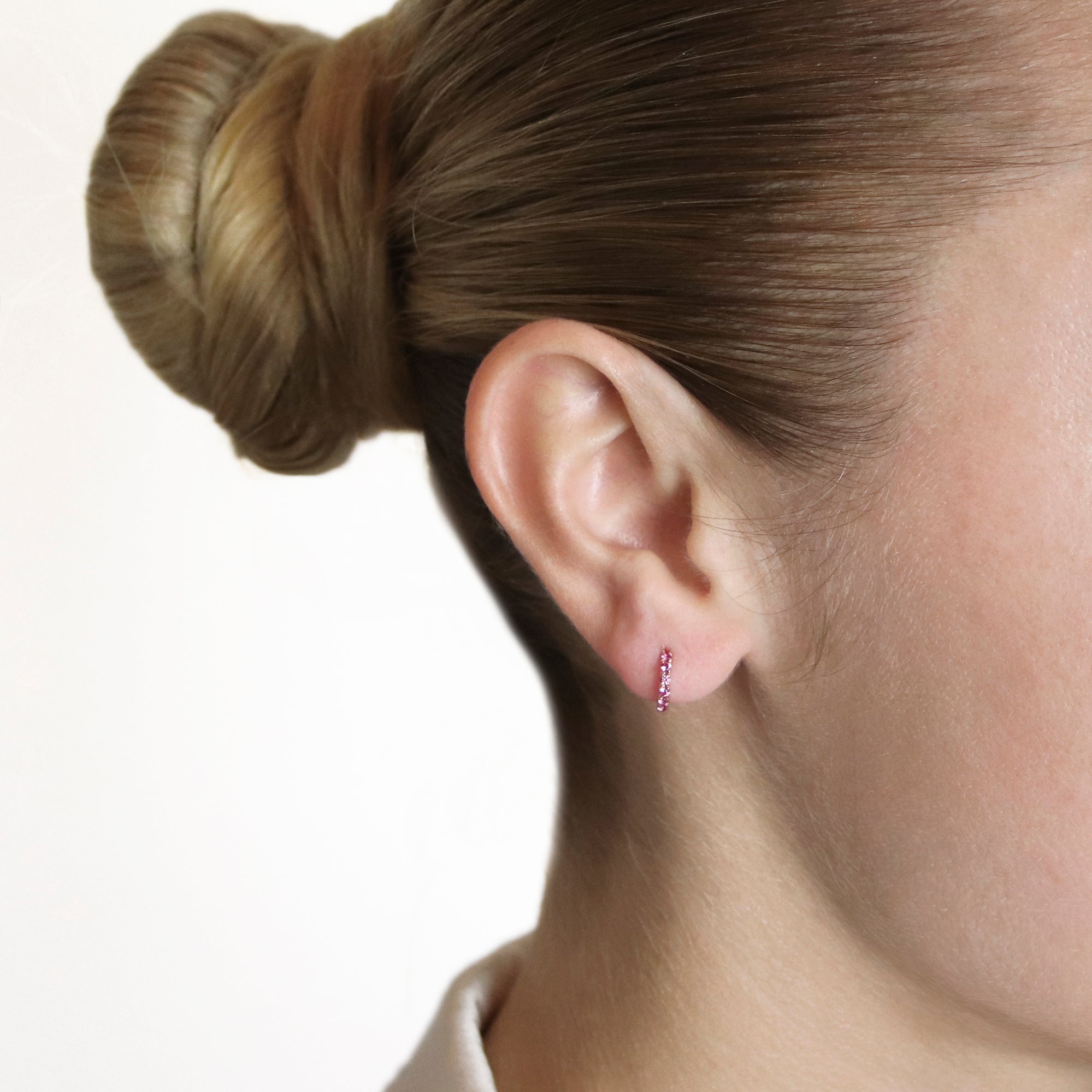 Pink sapphire huggie earrings in 18ct rose gold being worn